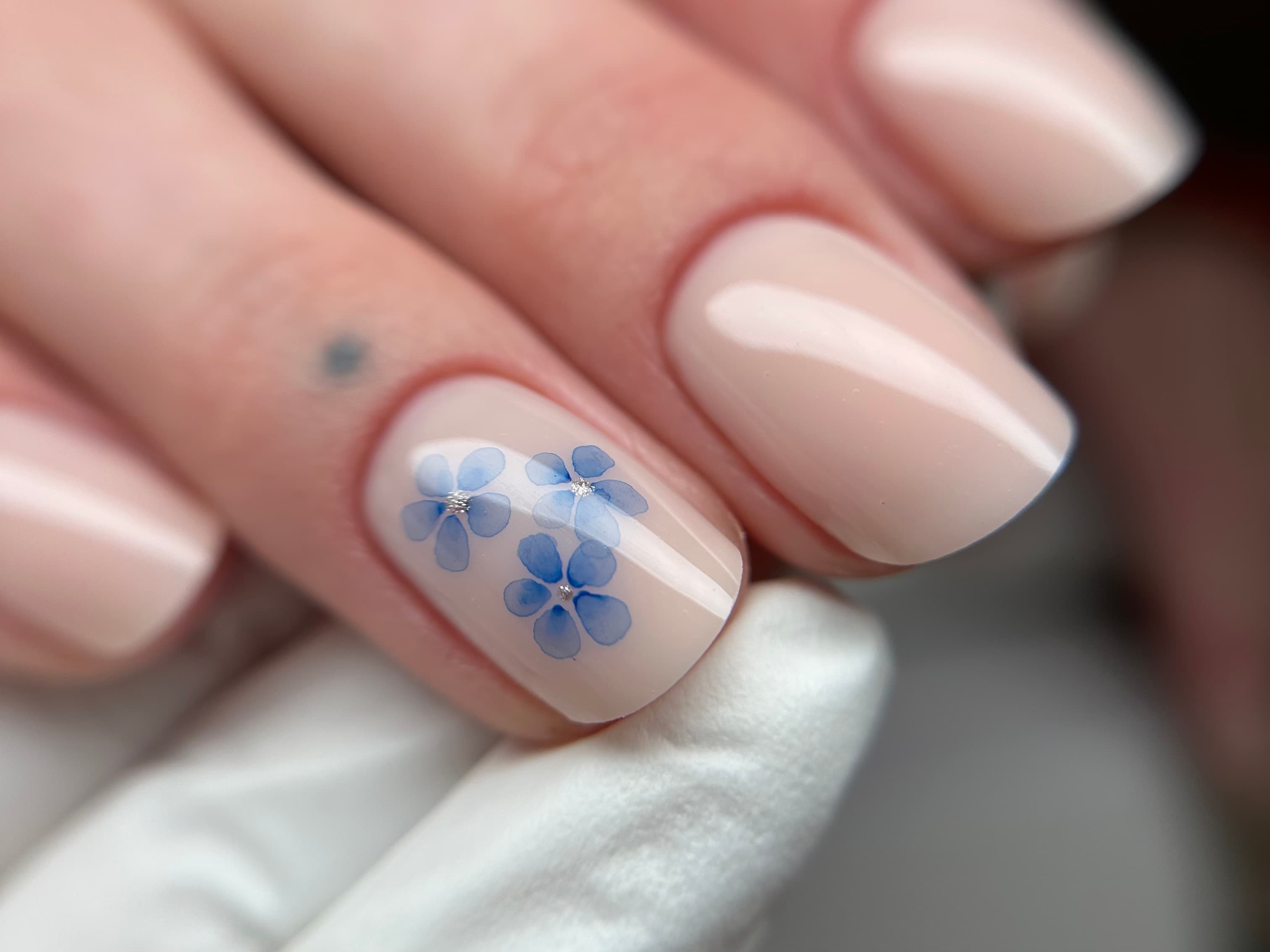 Glossy nude milky manicure with a hand-painted blue floral accent nail